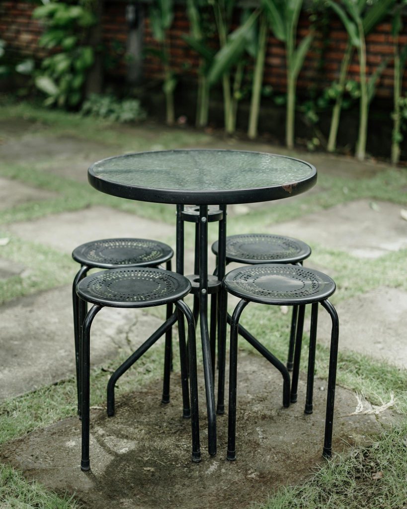 Modern outdoor garden patio set featuring round glass table and metal chairs, ideal for cafes.
